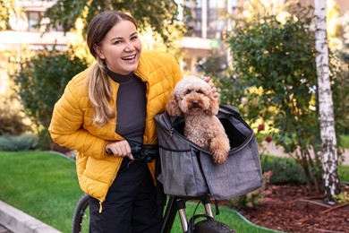 Woman with bicycle and cute Toy Poodle dog in pet carrier outdoors