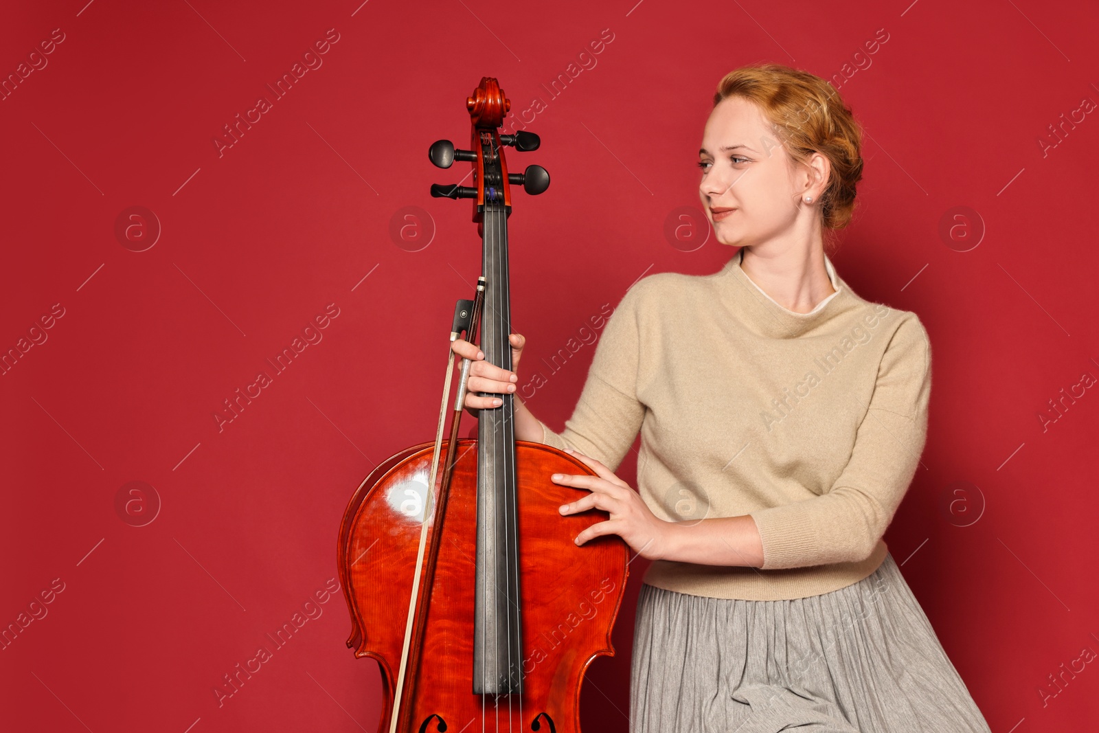 Photo of Beautiful young woman with cello on red background