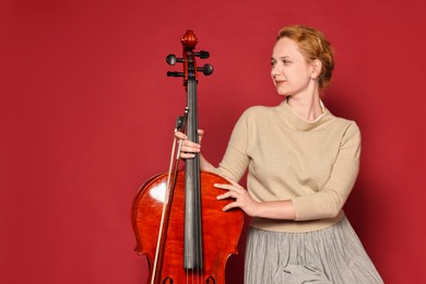 Photo of Beautiful young woman with cello on red background