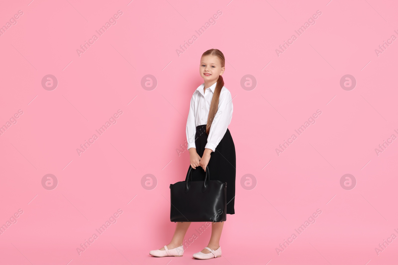 Photo of Little girl with bag pretending to be businesswoman on pink background. Dreaming of future profession