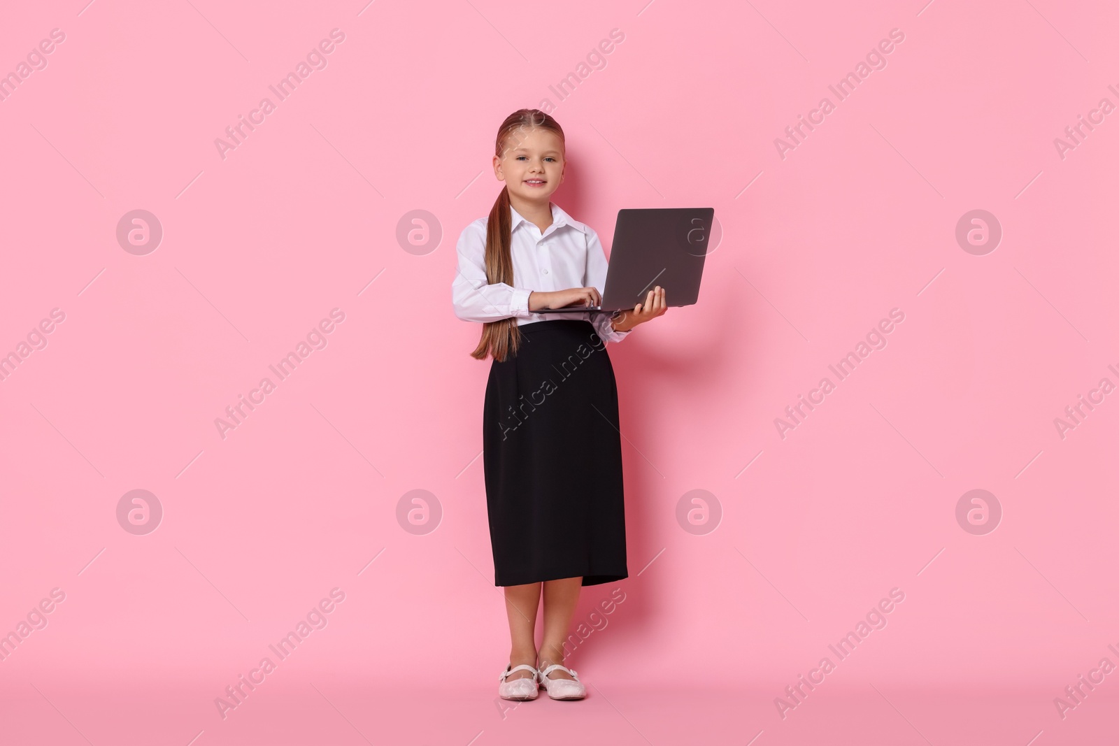 Photo of Little girl with laptop pretending to be accountant on pink background. Dreaming of future profession