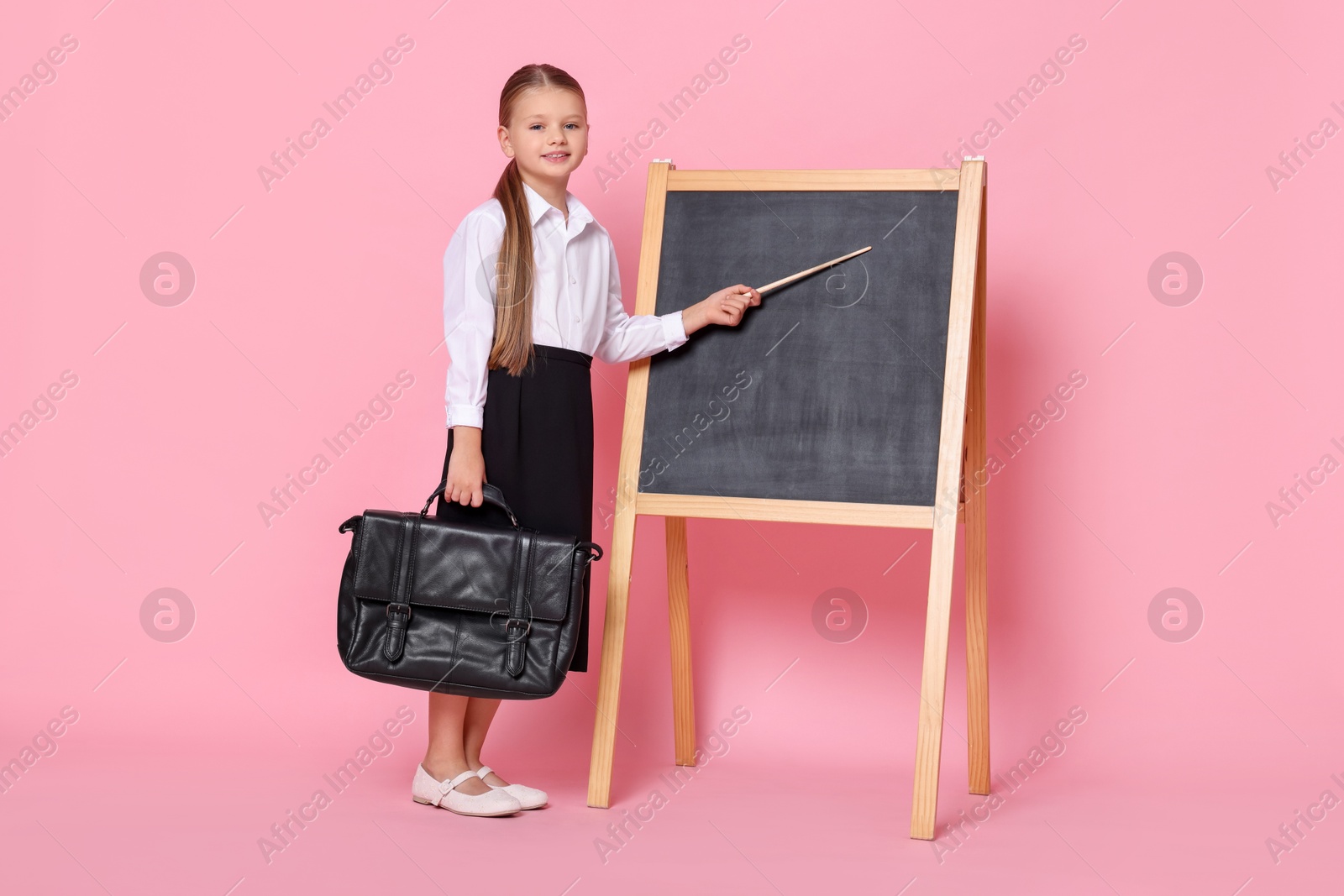 Photo of Little girl with pointer and briefcase near chalkboard pretending to be teacher on pink background. Dreaming about future profession