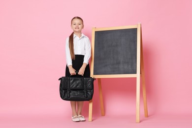 Photo of Little girl with briefcase near chalkboard pretending to be teacher on pink background. Dreaming about future profession