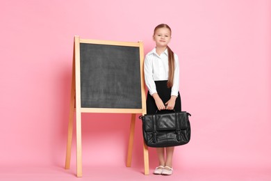 Photo of Little girl with briefcase near chalkboard pretending to be teacher on pink background. Dreaming about future profession