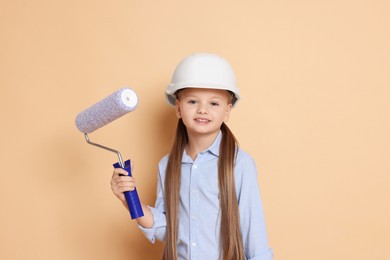 Photo of Little girl in hard hat with roller brush on beige background. Dreaming about future profession