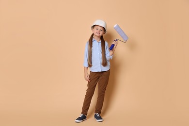 Photo of Little girl in hard hat with roller brush on beige background. Dreaming about future profession