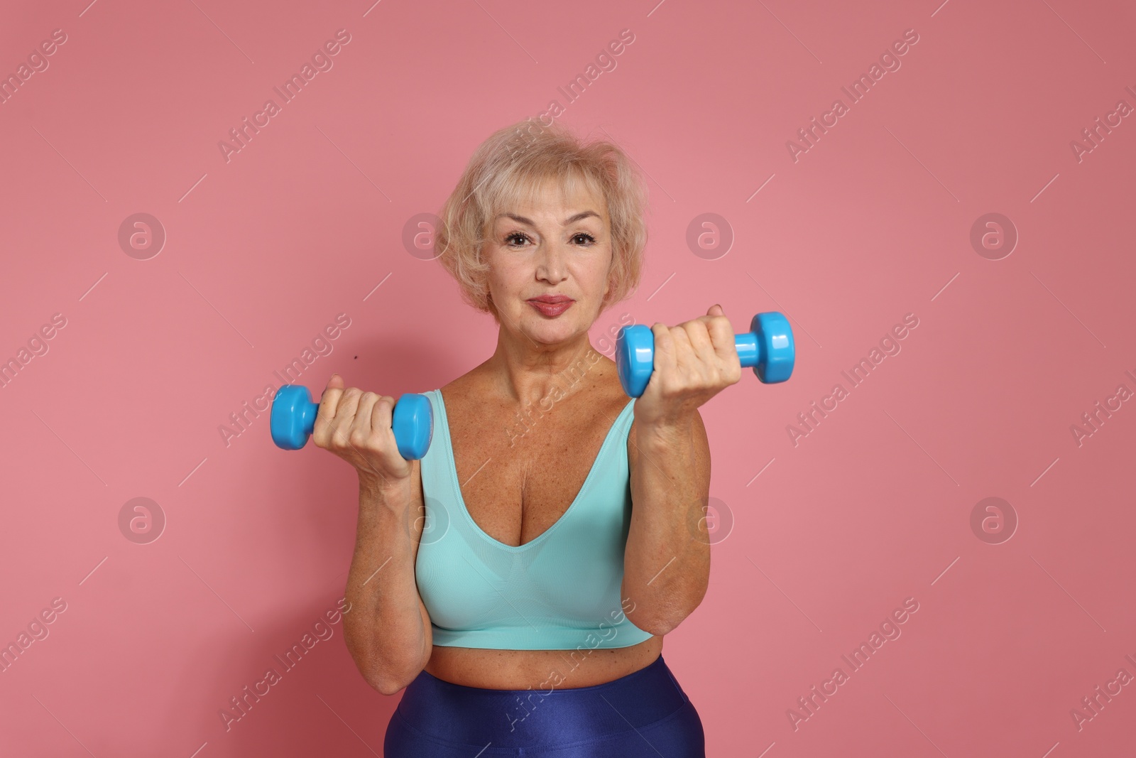 Photo of Senior woman exercising with dumbbells on pink background