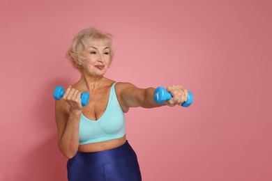 Photo of Senior woman exercising with dumbbells on pink background, space for text