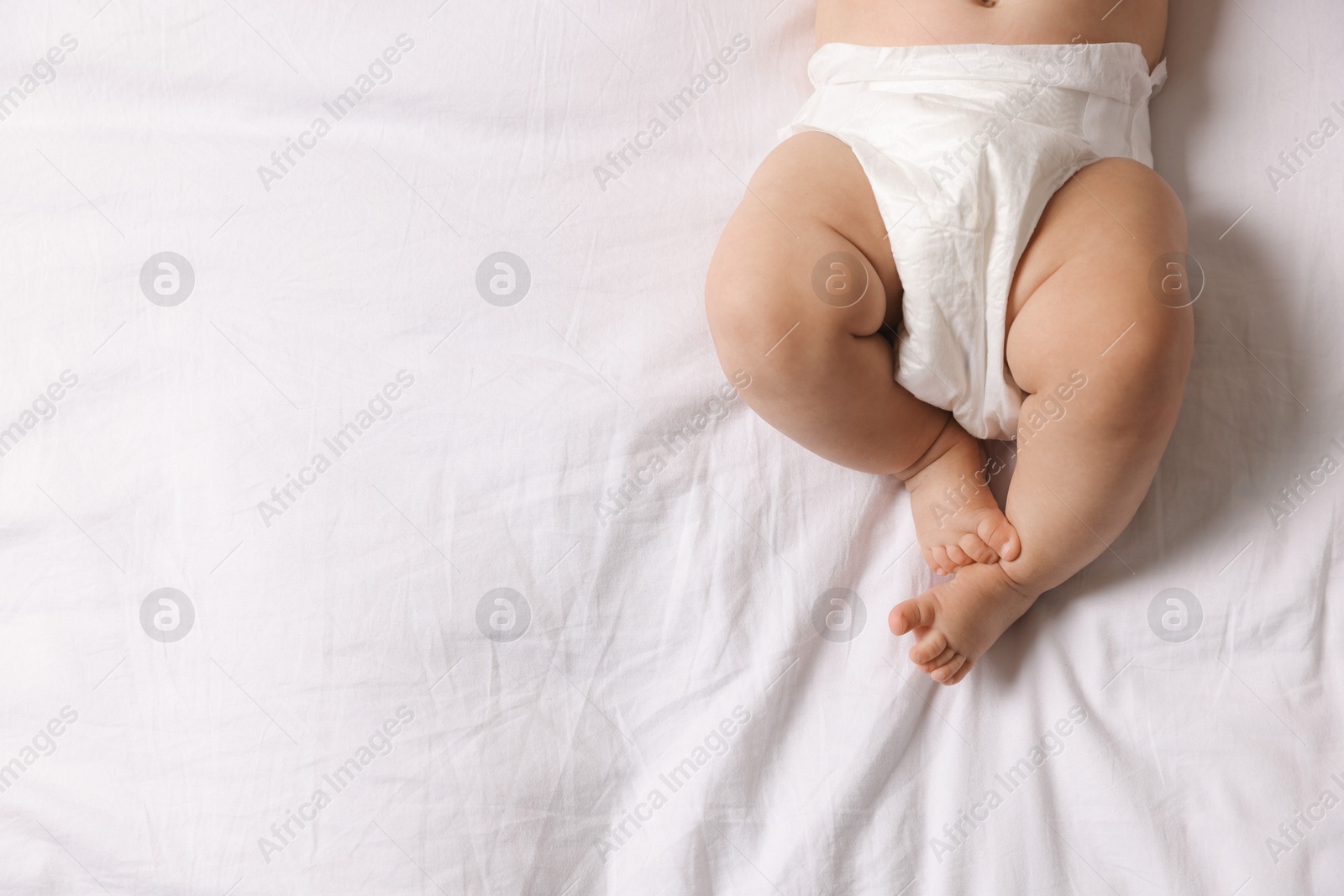 Photo of Cute little baby in diaper on bed, top view. Space for text