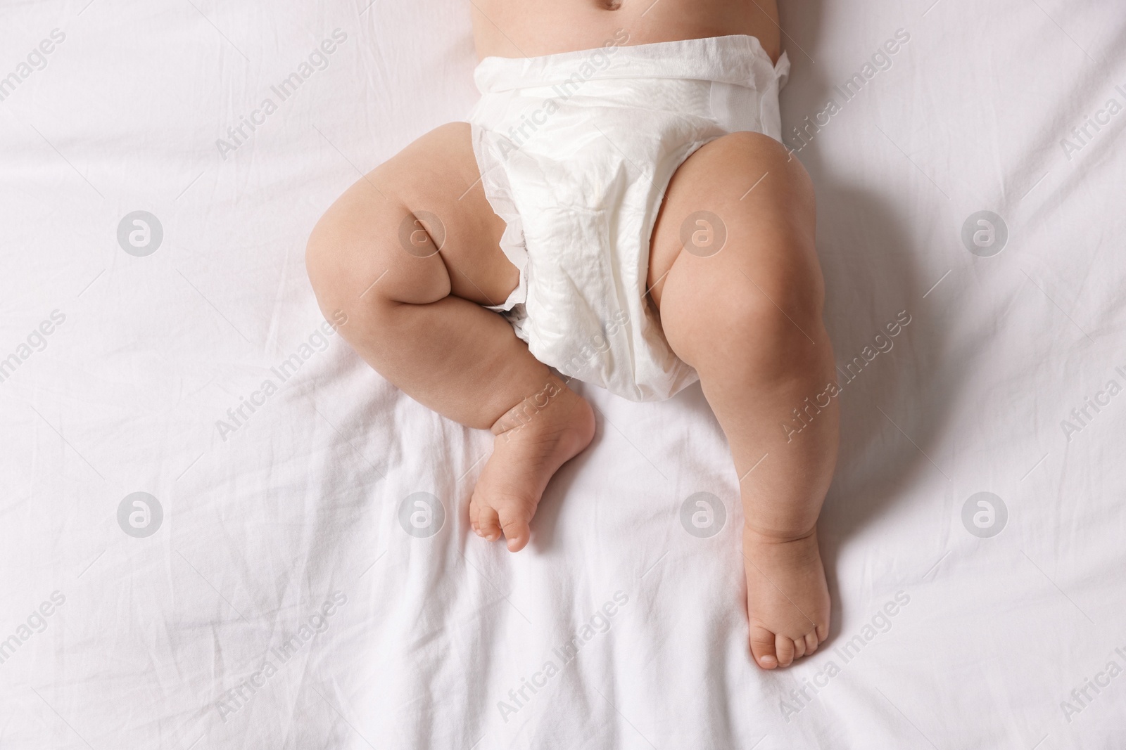 Photo of Cute little baby in diaper on bed, top view