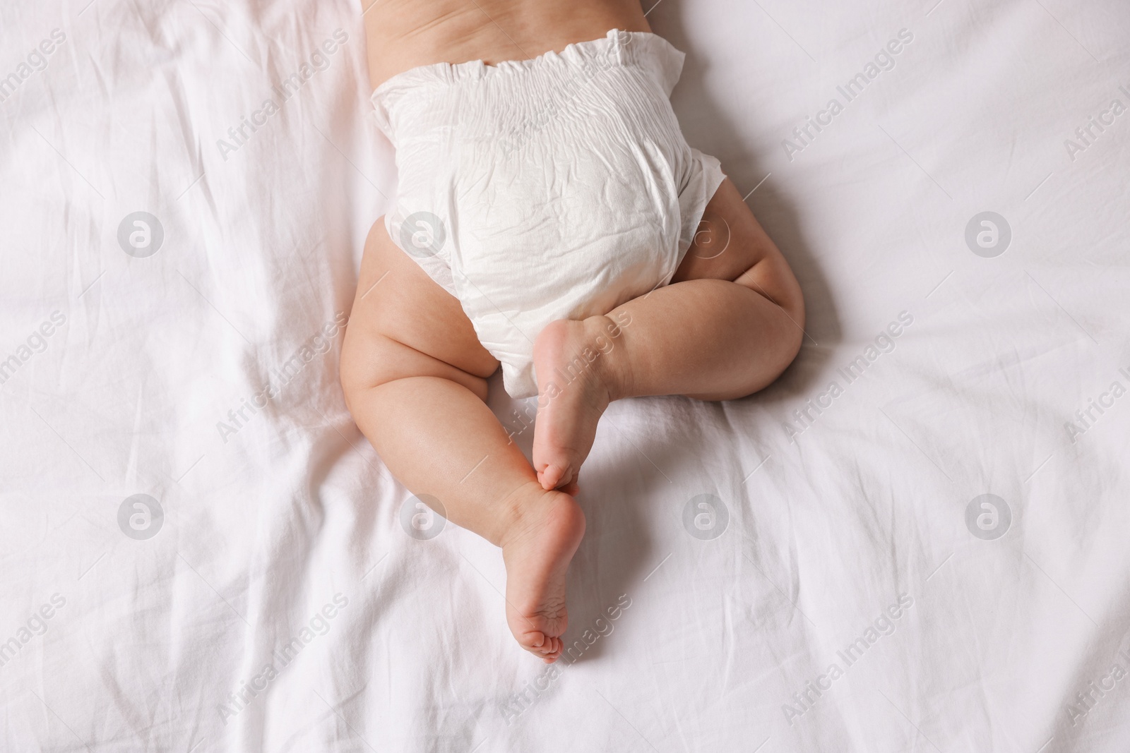 Photo of Cute little baby in diaper on bed, top view