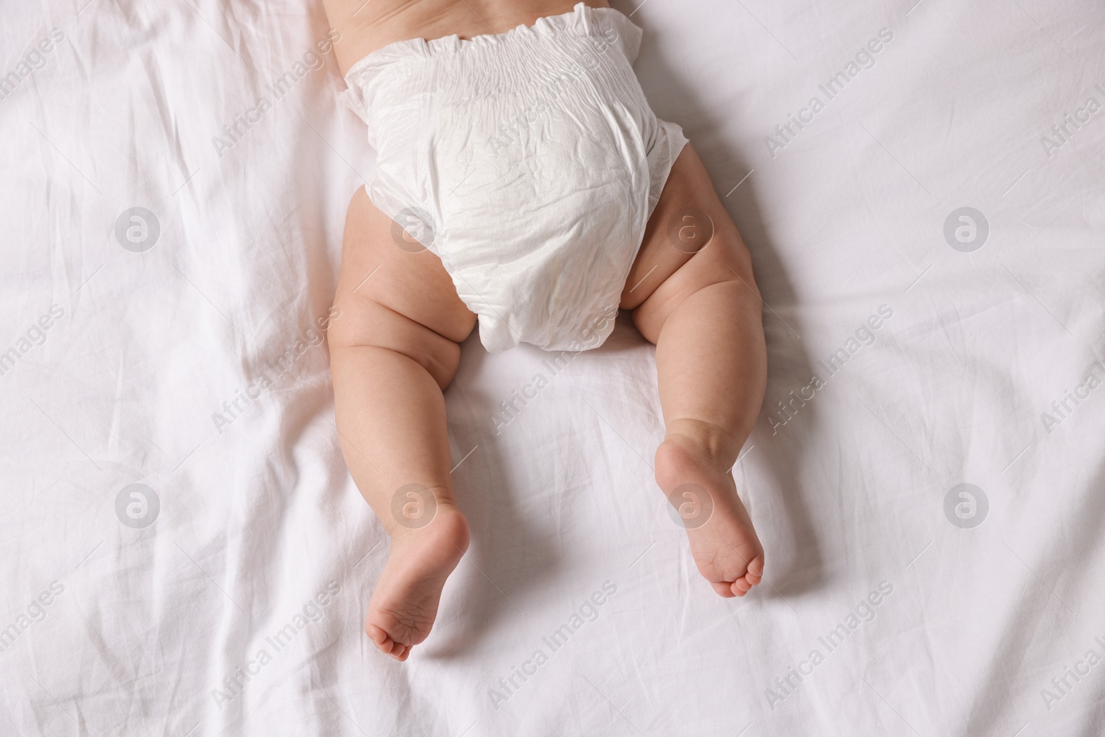 Photo of Cute little baby in diaper on bed, top view