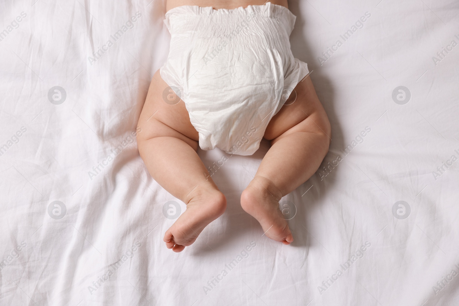 Photo of Cute little baby in diaper on bed, top view