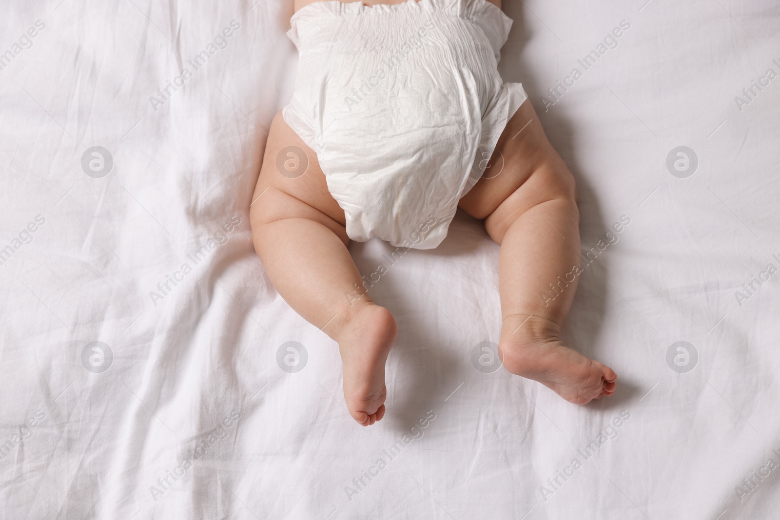 Photo of Cute little baby in diaper on bed, top view