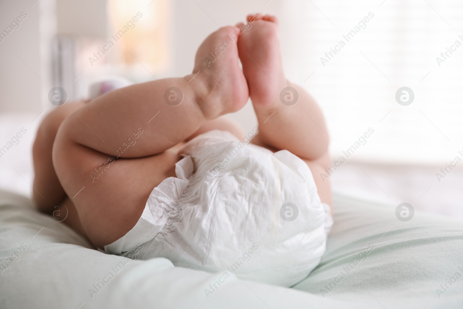 Photo of Cute little baby in diaper on bed indoors, closeup