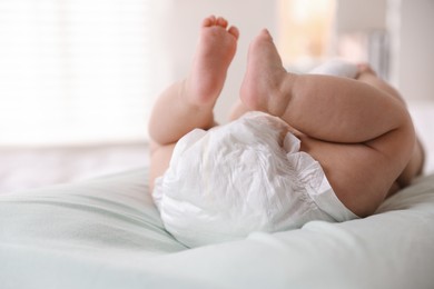 Photo of Cute little baby in diaper on bed indoors, closeup