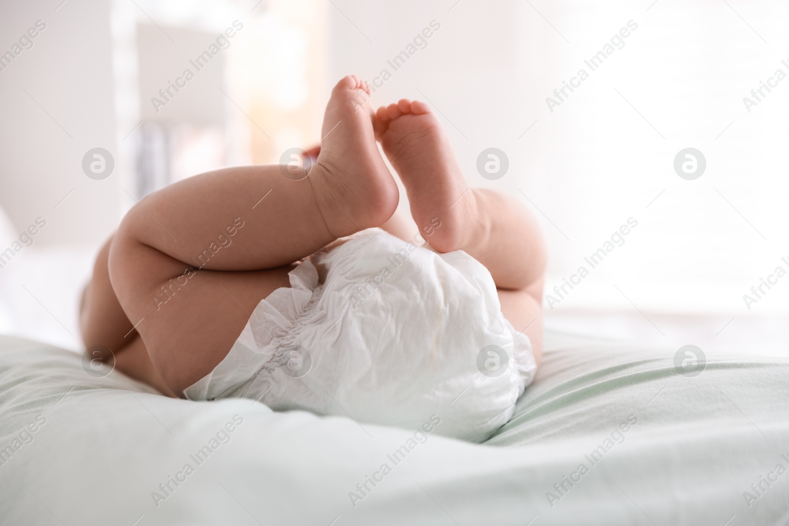 Photo of Cute little baby in diaper on bed indoors, closeup