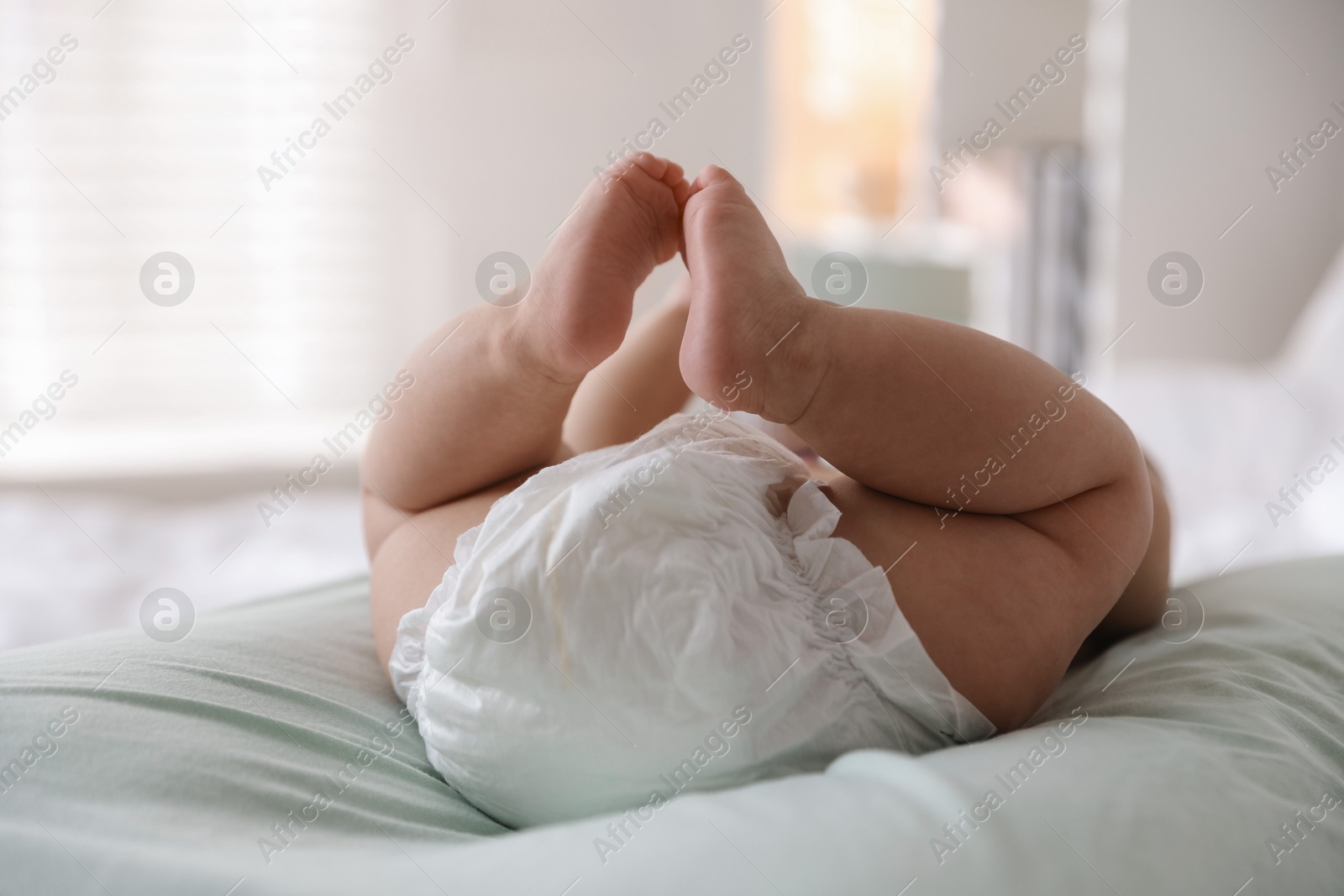 Photo of Cute little baby in diaper on bed indoors, closeup