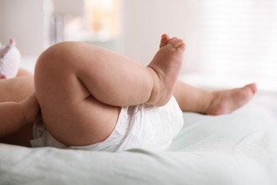 Photo of Cute little baby in diaper on bed indoors, closeup