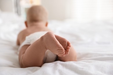 Cute little baby in diaper on bed indoors, selective focus. Space for text