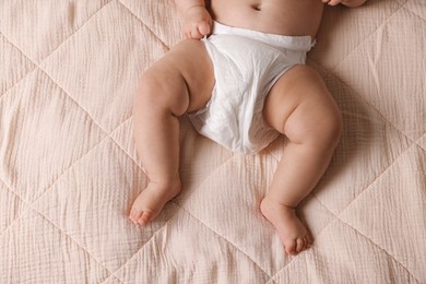 Photo of Cute little baby in diaper on bed, top view