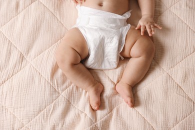 Cute little baby in diaper on bed, top view