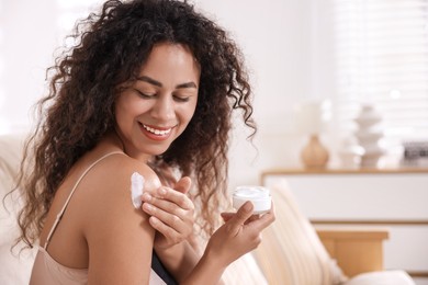 Photo of Young woman applying cream onto shoulder at home. Space for text