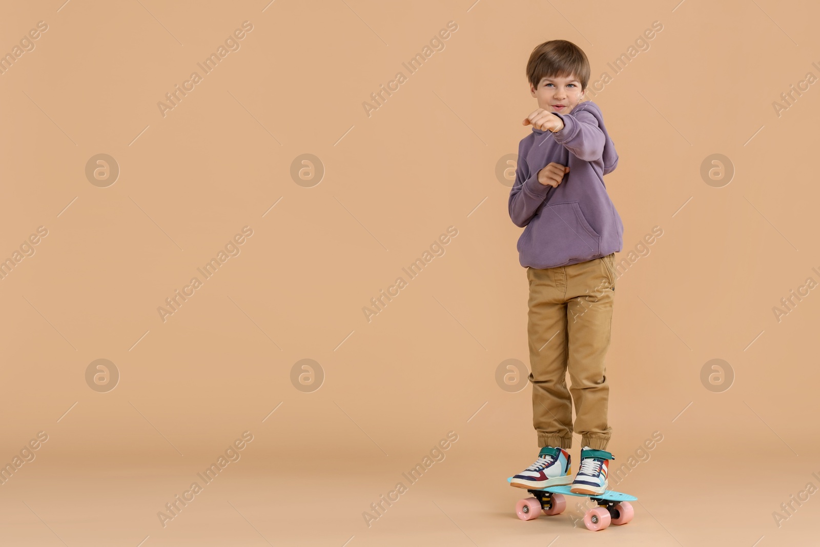 Photo of Little boy with skateboard on beige background, space for text