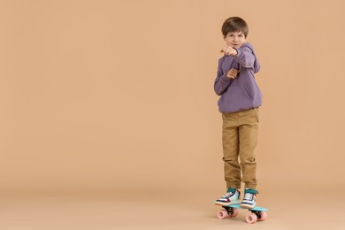 Photo of Little boy with skateboard on beige background, space for text