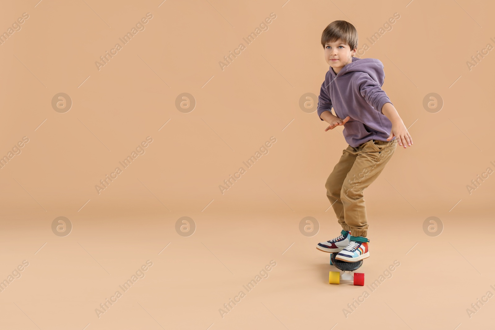 Photo of Little boy with skateboard on beige background, space for text