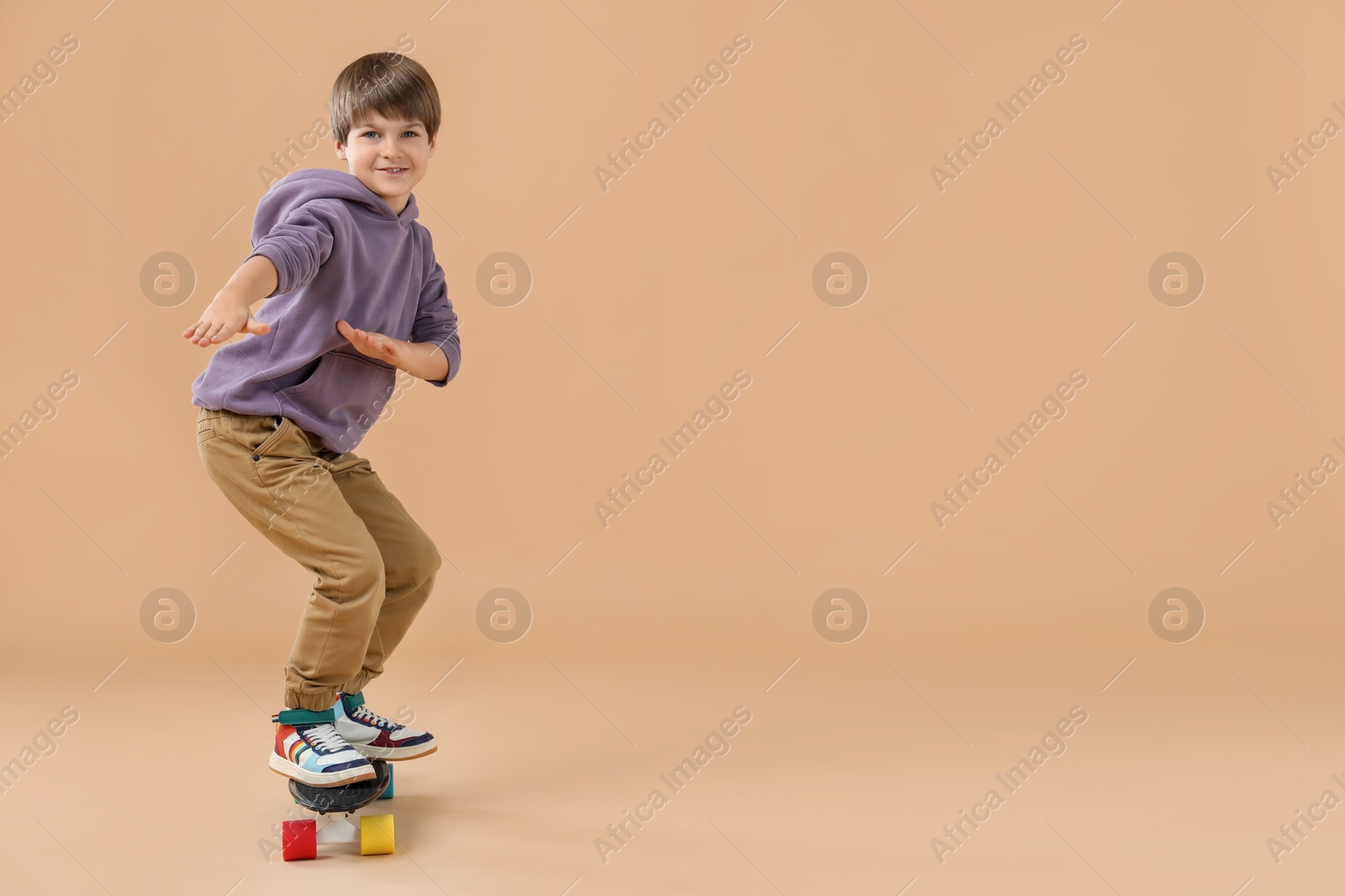 Photo of Little boy with skateboard on beige background, space for text