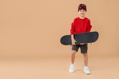 Photo of Little boy with skateboard on beige background, space for text