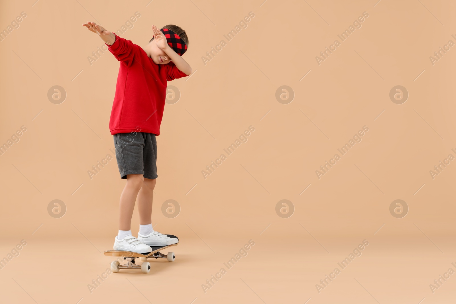 Photo of Little boy with skateboard on beige background, space for text