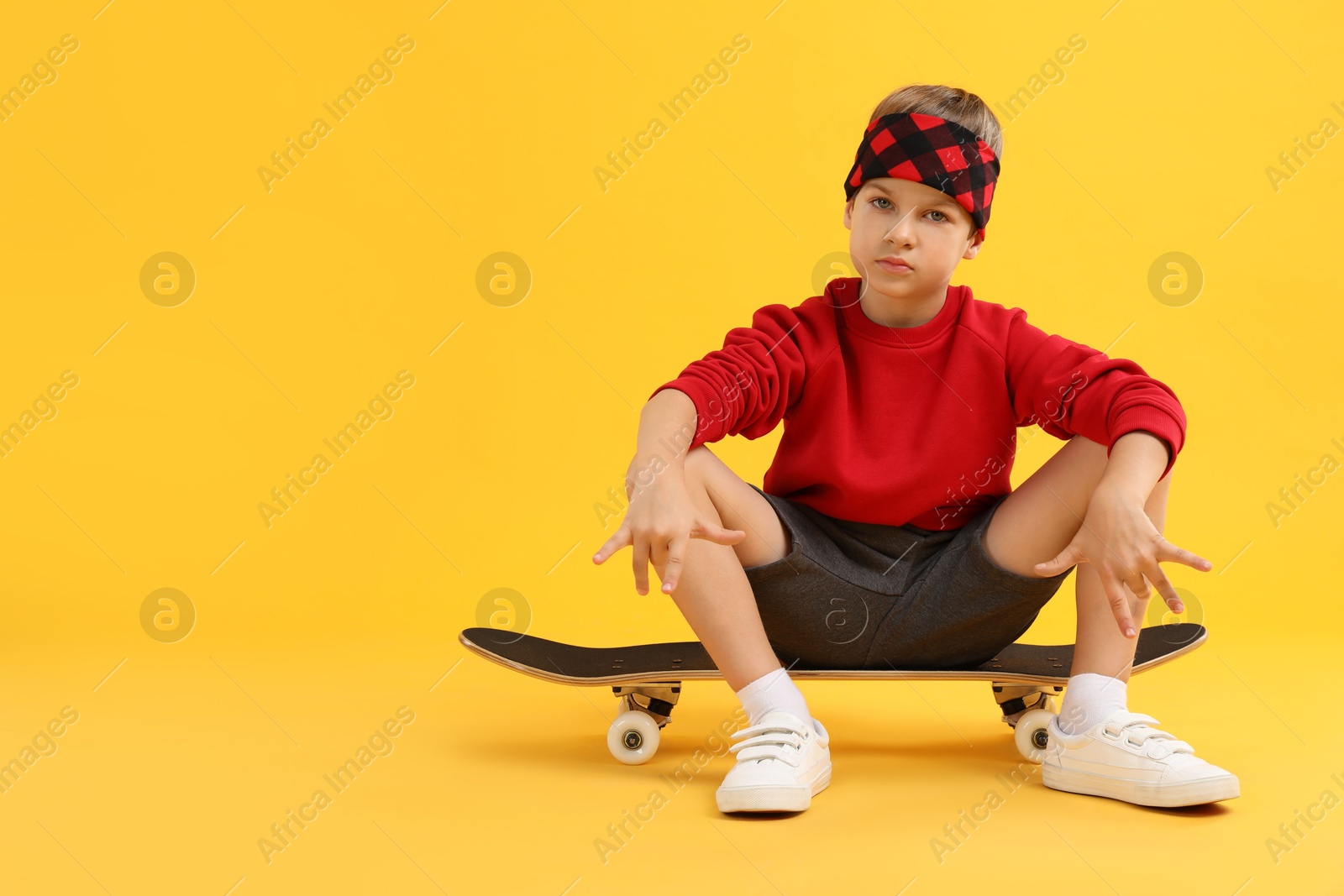 Photo of Little boy with skateboard on yellow background, space for text