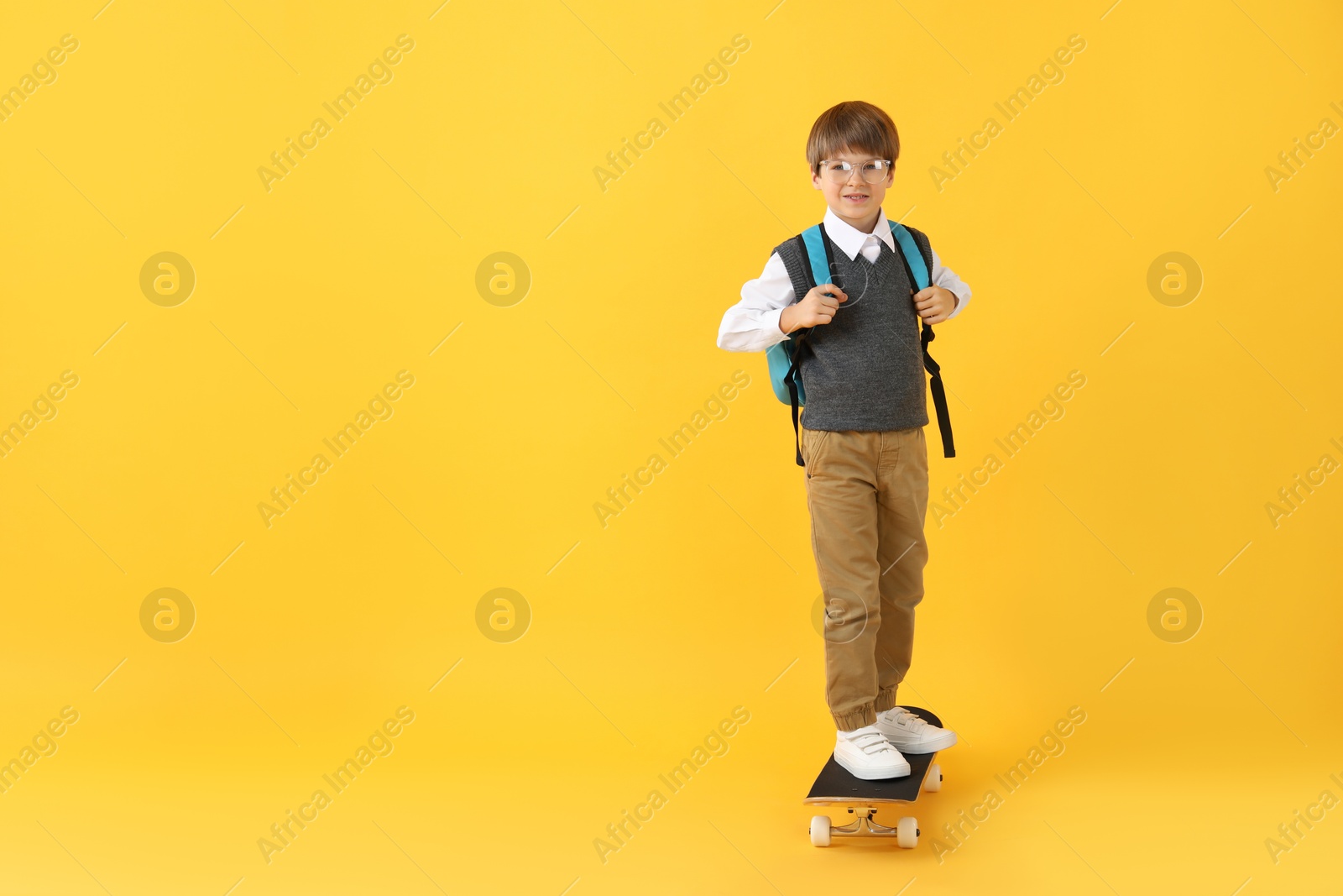 Photo of Little boy with skateboard on yellow background, space for text