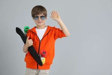 Photo of Little boy with skateboard on light grey background, space for text