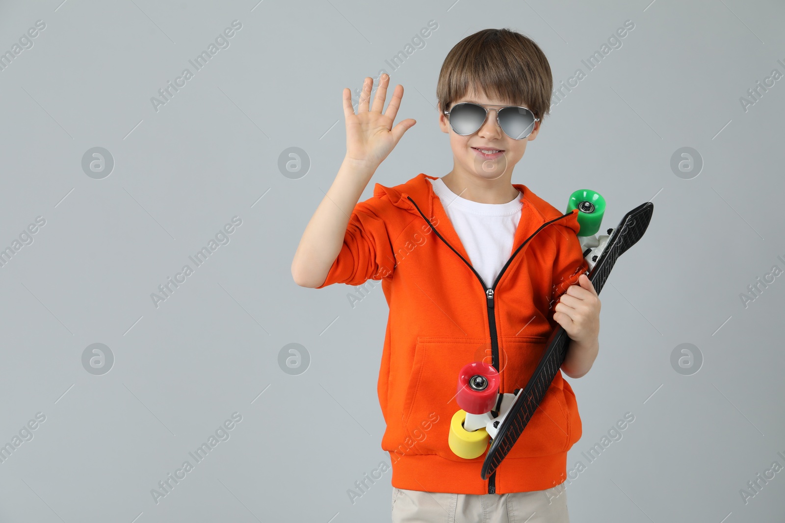 Photo of Little boy with skateboard on light grey background, space for text