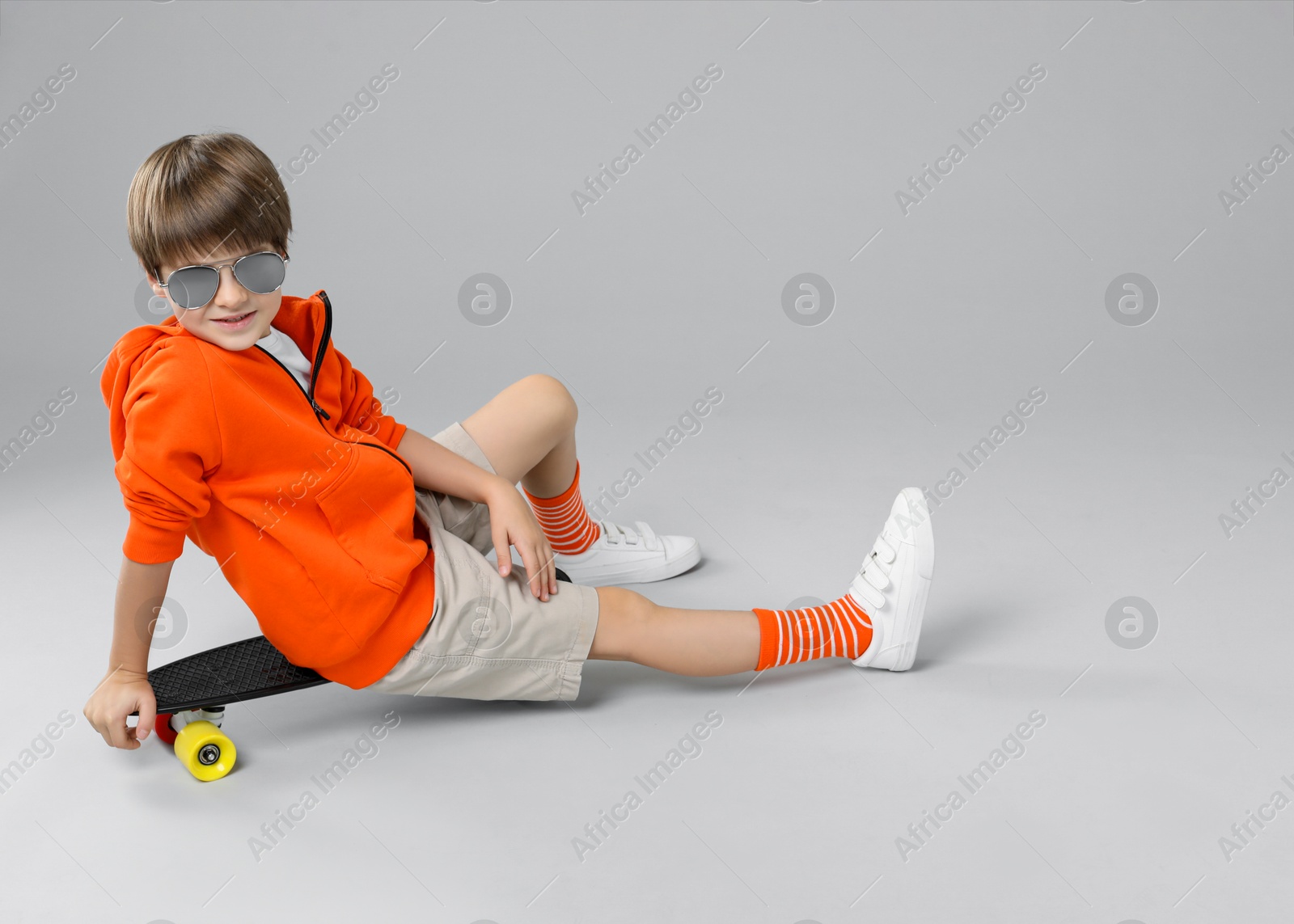 Photo of Little boy with skateboard on light grey background, space for text