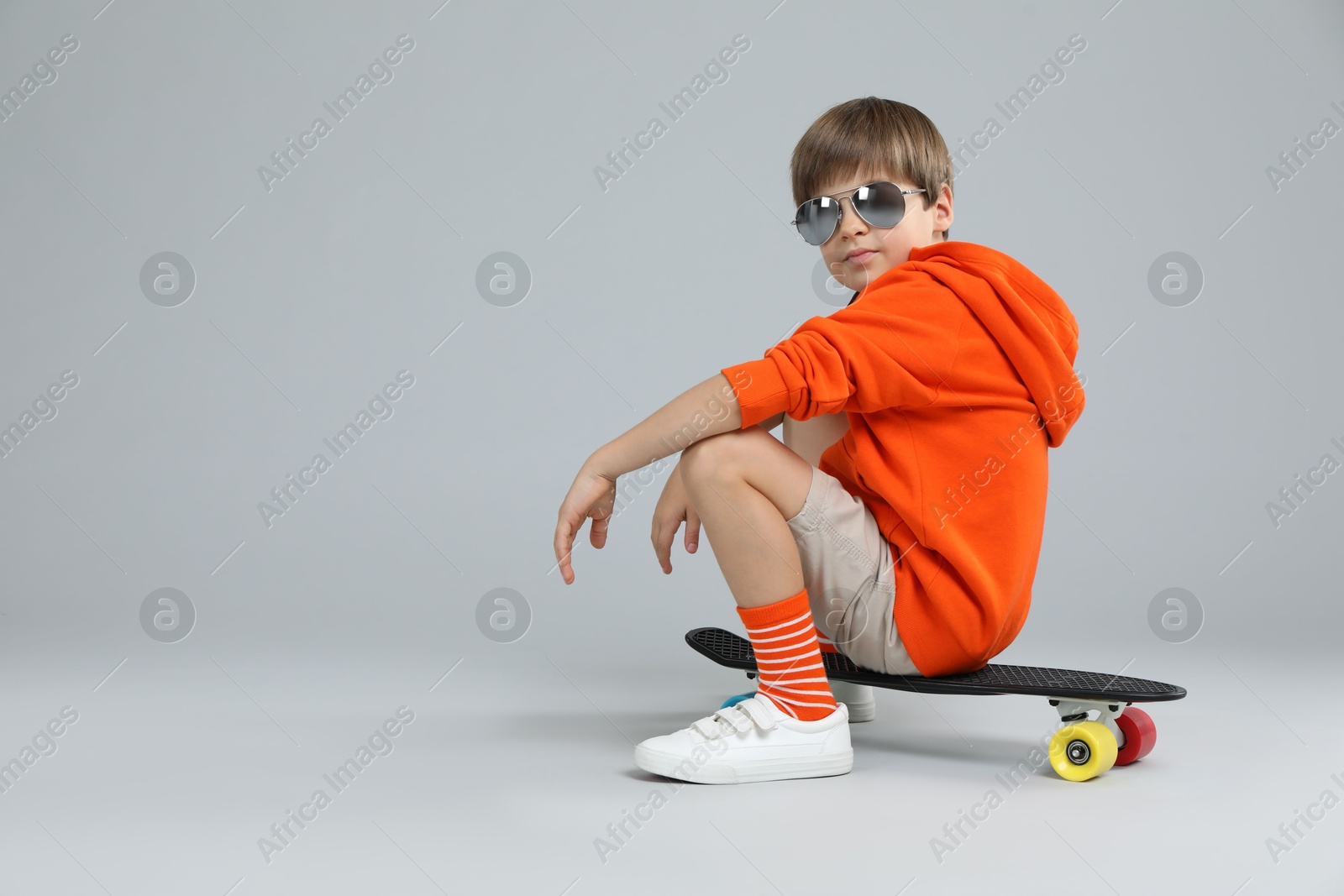 Photo of Little boy with skateboard on light grey background, space for text