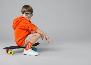 Photo of Little boy with skateboard on light grey background, space for text