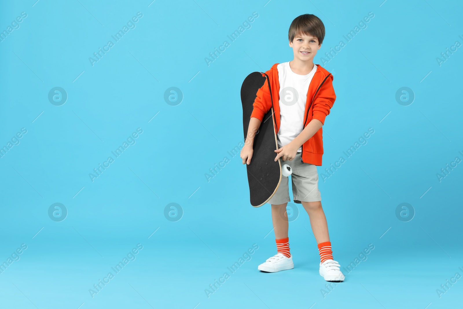 Photo of Little boy with skateboard on light blue background, space for text