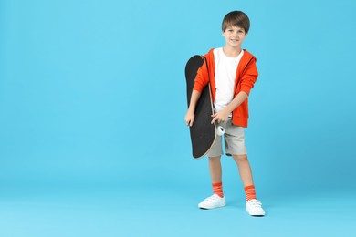 Photo of Little boy with skateboard on light blue background, space for text