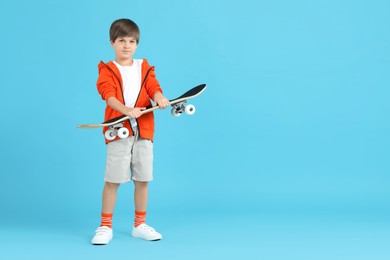 Photo of Little boy with skateboard on light blue background, space for text