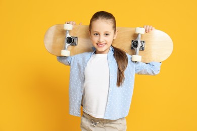 Stylish girl with skateboard on yellow background