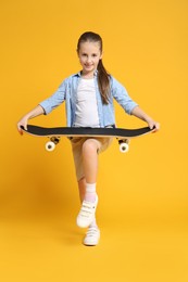 Stylish girl with skateboard on yellow background