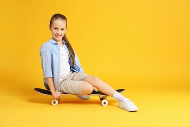 Photo of Stylish girl sitting on skateboard against yellow background, space for text