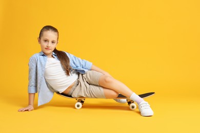 Stylish girl sitting on skateboard against yellow background. Space for text