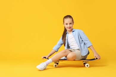 Photo of Stylish girl sitting on skateboard against yellow background, space for text