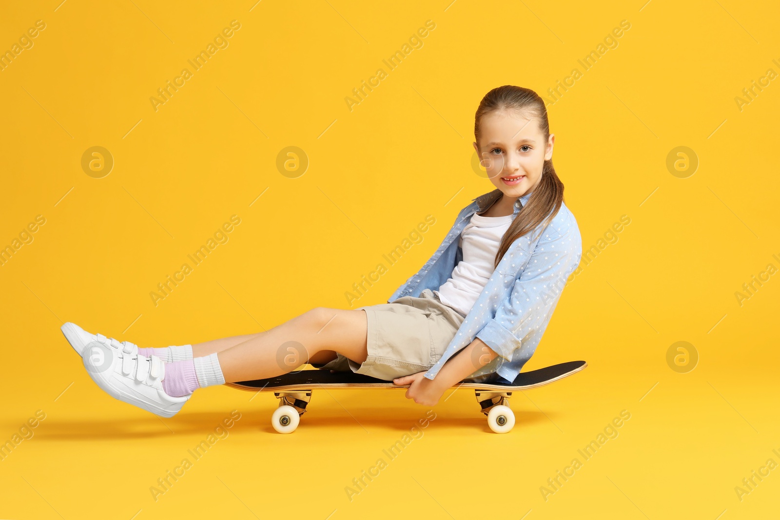 Photo of Stylish girl sitting on skateboard against yellow background