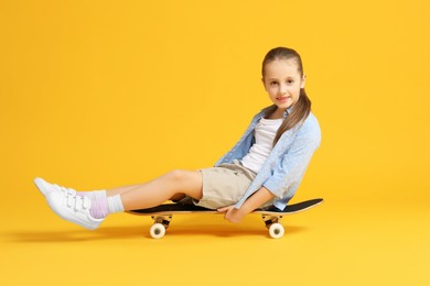 Stylish girl sitting on skateboard against yellow background